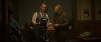 Movie still from “Stockholm” (2018), directed by Robert Budreau – Two men standing next to each other in front of a window; Medium shot, Low angle