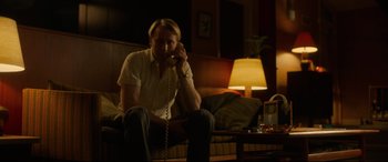 Movie still from “Stockholm” (2018), directed by Robert Budreau – A man sitting on a couch talking on a phone; Medium shot, Low angle