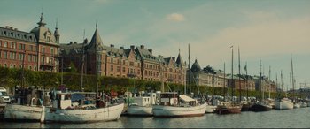 Movie still from “Stockholm” (2018), directed by Robert Budreau – A group of boats in the water in front of a large building; Extreme Wide shot, Low angle