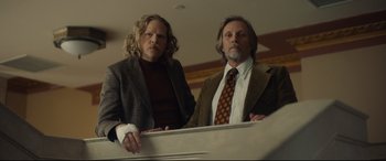 Movie still from “Stockholm” (2018), directed by Robert Budreau – A couple of men standing next to each other in a room; Medium shot, Low angle