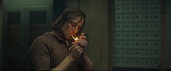 Movie still from “Stockholm” (2018), directed by Robert Budreau – A man is lighting a cigarette in a dark room; Medium shot, Low angle