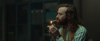 Movie still from “Stockholm” (2018), directed by Robert Budreau – A man with a beard is lighting a cigarette; Close Up shot, Over the shoulder angle