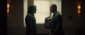 Movie still from “Stockholm” (2018), directed by Robert Budreau – Two people standing next to each other in front of a window; Medium shot, Over the shoulder angle