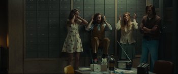 Movie still from “Stockholm” (2018), directed by Robert Budreau – A man and two women are sitting in front of a wall of lockers; Medium shot, Low angle