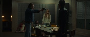 Movie still from “Stockholm” (2018), directed by Robert Budreau – A man holding a gun pointed at a woman in front of a group of people; Wide shot, Over the shoulder angle