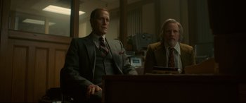 Movie still from “Stockholm” (2018), directed by Robert Budreau – Two men in suits sitting at a table; Medium shot, Low angle