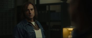 Movie still from “Stockholm” (2018), directed by Robert Budreau – A man with long dark hair wearing a jean jacket; Medium shot, Over the shoulder angle