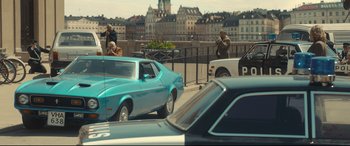 Movie still from “Stockholm” (2018), directed by Robert Budreau – A couple of cars parked on the side of a road; Wide shot, Over the shoulder angle