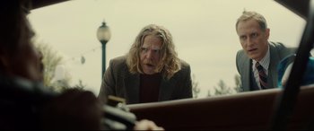 Movie still from “Stockholm” (2018), directed by Robert Budreau – A man with long blonde hair and a beard is looking at the camera; Medium shot, Over the shoulder angle