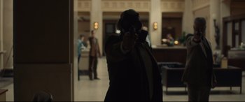 Movie still from “Stockholm” (2018), directed by Robert Budreau – A man in a suit and tie holding a gun in a room; Wide shot, Over the shoulder angle