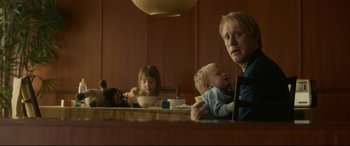 Movie still from “Stockholm” (2018), directed by Robert Budreau – A woman and two children sitting at a dining table; Medium shot, Over the shoulder angle