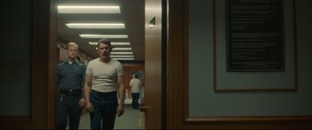 Movie still from “Stockholm” (2018), directed by Robert Budreau – A man standing in front of a door in a room; Medium shot, Low angle