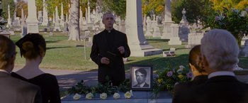 Movie still from “Stoker” (2013), directed by Park Chan-wook – A priest standing in front of a photo of a deceased person; Medium shot, Over the shoulder angle