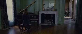 A woman sitting in front of a grand piano in front of a fire place