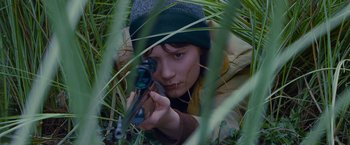 Movie still from “Stoker” (2013), directed by Park Chan-wook – A person with a rifle in the grass; Close Up shot, High angle