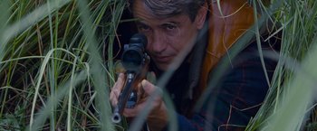 Movie still from “Stoker” (2013), directed by Park Chan-wook – A man is holding a rifle in the grass; Close Up shot, High angle