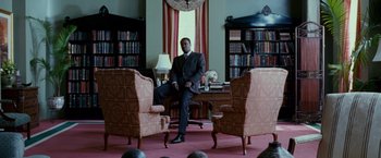 Movie still from “Stomp the Yard” (2007), directed by Sylvain White – A man in a suit sitting at a desk in front of two chairs; Wide shot, Low angle