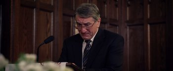 Movie still from “Stone” (2010), directed by John Curran – An older man wearing a suit and reading a book; Close Up shot, Over the shoulder angle