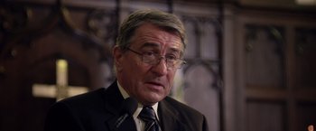 Movie still from “Stone” (2010), directed by John Curran – An older man wearing glasses and a suit; Close Up shot, Over the shoulder angle