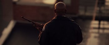Movie still from “Stone” (2010), directed by John Curran – A bald man in a black jacket holding a gun; Medium shot, Over the shoulder angle