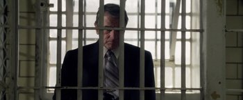 Movie still from “Stone” (2010), directed by John Curran – A man in a suit and tie behind bars in a jail cell; Medium shot, Low angle