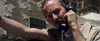 Movie still from “Stone” (2010), directed by John Curran – A man holding a phone up to his ear while standing in front of a building; Close Up shot, Low angle