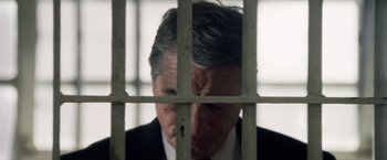 Movie still from “Stone” (2010), directed by John Curran – A man in a suit and tie behind bars; Close Up shot, Low angle