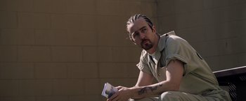 Movie still from “Stone” (2010), directed by John Curran – A man sitting on the side of a wall holding a book; Close Up shot, Over the shoulder angle