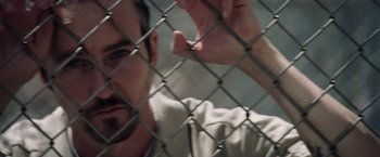 Movie still from “Stone” (2010), directed by John Curran – A man is behind a chain link fence; Close Up shot, Over the shoulder angle