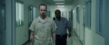 Movie still from “Stone” (2010), directed by John Curran – A man in a prison uniform is walking down a hallway with another man; Medium shot, Low angle