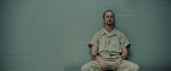 Movie still from “Stone” (2010), directed by John Curran – A man sitting on a bench in a jail cell; Medium shot, Low angle
