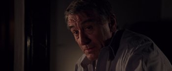 Movie still from “Stone” (2010), directed by John Curran – An older man looking at the camera in a dimly - lit room; Close Up shot, Over the shoulder angle