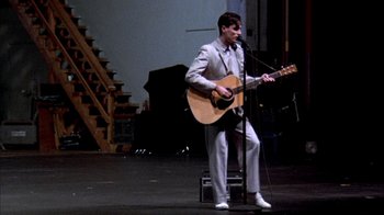 Movie still from “Stop Making Sense” (1984), directed by Jonathan Demme – A man in a suit playing an instrument on stage; Wide shot, Low angle