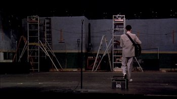 Movie still from “Stop Making Sense” (1984), directed by Jonathan Demme – A man in a white suit is walking on stage; Wide shot, Low angle