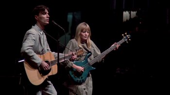 Movie still from “Stop Making Sense” (1984), directed by Jonathan Demme – A man and a woman holding guitars on a stage; Medium shot, Low angle