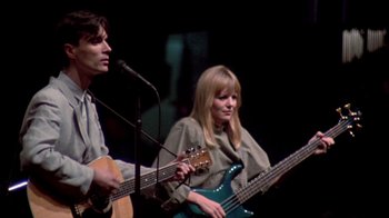 Movie still from “Stop Making Sense” (1984), directed by Jonathan Demme – A man and a woman are playing guitar and singing; Medium shot, Low angle