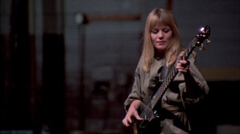 Movie still from “Stop Making Sense” (1984), directed by Jonathan Demme – A woman is playing an electric guitar in a dark room; Medium shot, Low angle