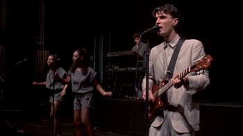 Movie still from “Stop Making Sense” (1984), directed by Jonathan Demme – A group of people on a stage singing and playing guitar; Medium shot, Low angle