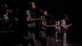 Movie still from “Stop Making Sense” (1984), directed by Jonathan Demme – A group of young people singing on stage; Wide shot, High angle