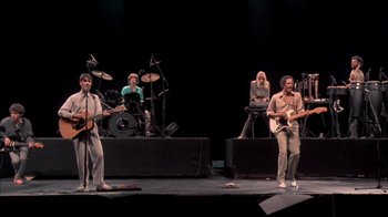 Movie still from “Stop Making Sense” (1984), directed by Jonathan Demme – A group of people on a stage playing instruments; Wide shot, High angle