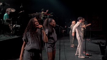 Movie still from “Stop Making Sense” (1984), directed by Jonathan Demme – A group of people on a stage with microphones; Wide shot, High angle