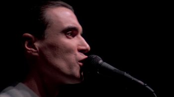 Movie still from “Stop Making Sense” (1984), directed by Jonathan Demme – A person singing into a microphone; Close Up shot, Low angle