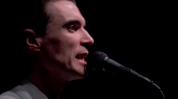 Movie still from “Stop Making Sense” (1984), directed by Jonathan Demme – A person holding a microphone; Close Up shot, High angle