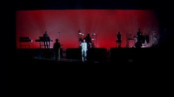 Movie still from “Stop Making Sense” (1984), directed by Jonathan Demme – A group of people standing on top of a stage; Extreme Wide shot, High angle