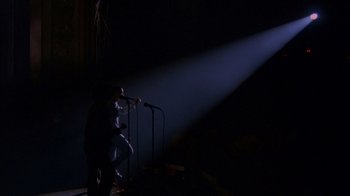 Movie still from “Stop Making Sense” (1984), directed by Jonathan Demme – A man standing on a stage with a microphone; Extreme Wide shot, Low angle