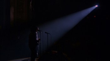Movie still from “Stop Making Sense” (1984), directed by Jonathan Demme – A man standing in front of two microphones on a stage; Extreme Wide shot, Low angle