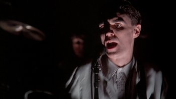 Movie still from “Stop Making Sense” (1984), directed by Jonathan Demme – A man with a microphone in a dark room; Close Up shot, Low angle