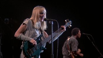 Movie still from “Stop Making Sense” (1984), directed by Jonathan Demme – A woman playing a bass guitar on a stage; Medium shot, Low angle
