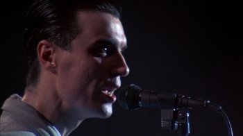 Movie still from “Stop Making Sense” (1984), directed by Jonathan Demme – A person singing into a microphone; Close Up shot, Low angle