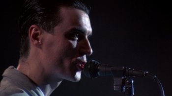 Movie still from “Stop Making Sense” (1984), directed by Jonathan Demme – A person holding a microphone; Close Up shot, Low angle